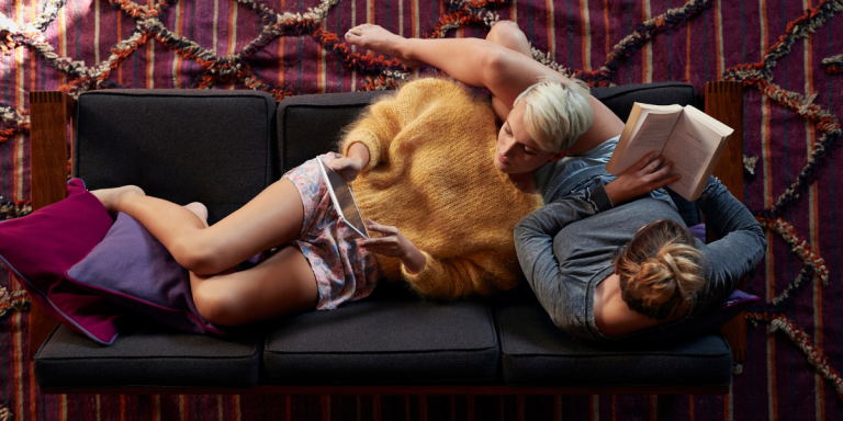Two lesbian recline while reading on their couch
