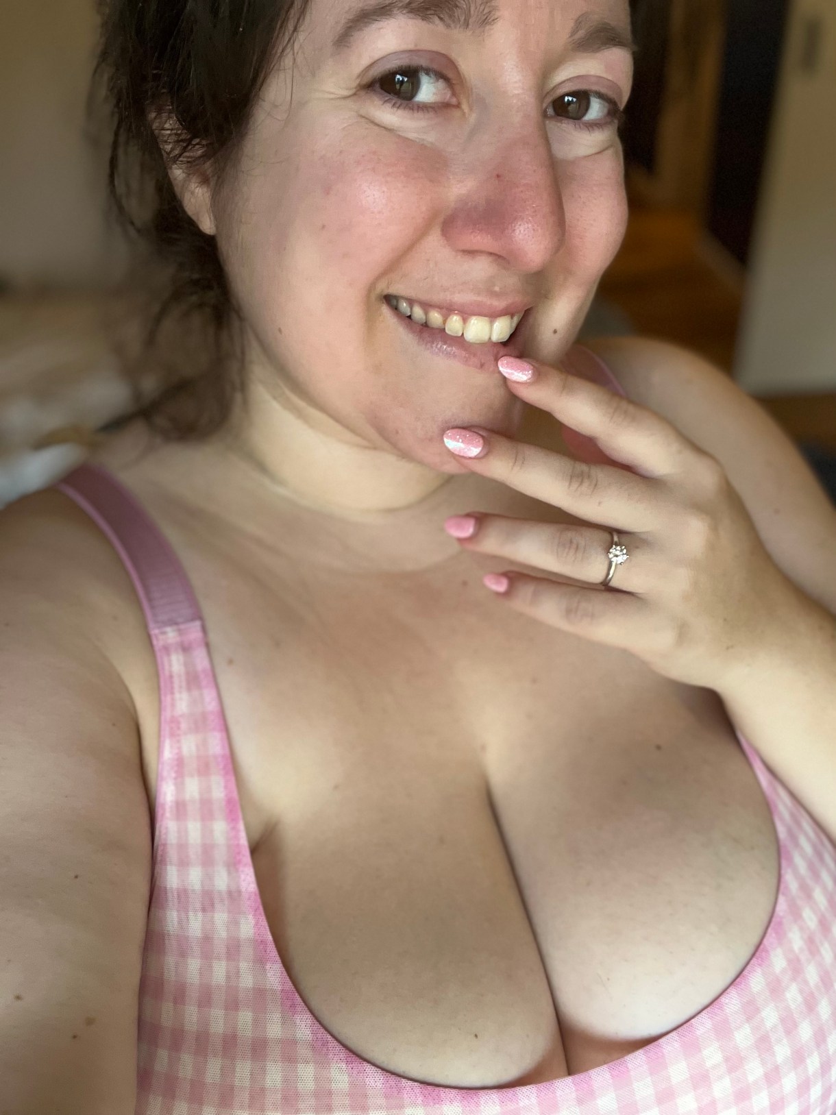 Vanessa is a white woman with brown hair who here is smiling in a pink gingham swimsuit top while showing off pink nails and her engagement ring