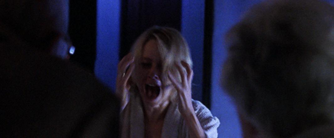 Naomi Watts screams with her hands to her face as two older people approach her.