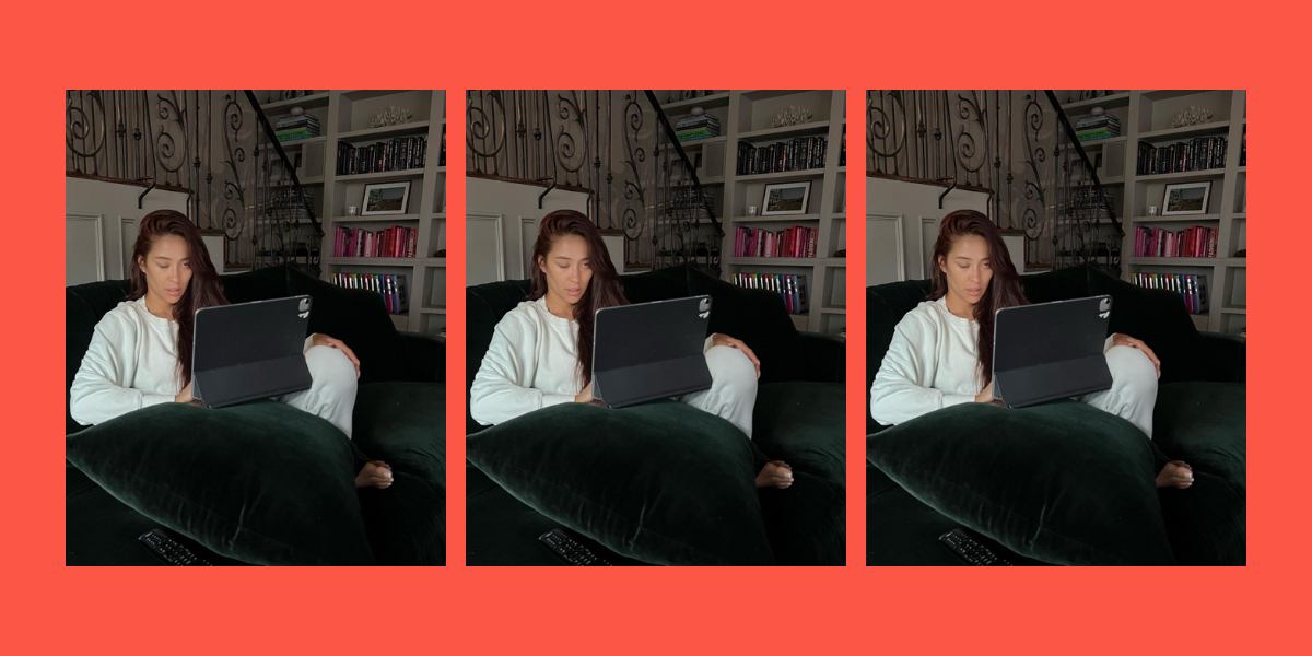 Shay Mitchell sits on a velvet green couch on her iPad making a face with her tongue out.