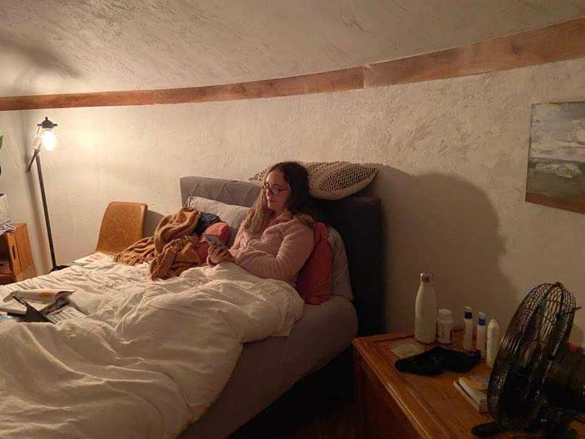 Anya, a white woman with long brown hair, relaxes in a bed