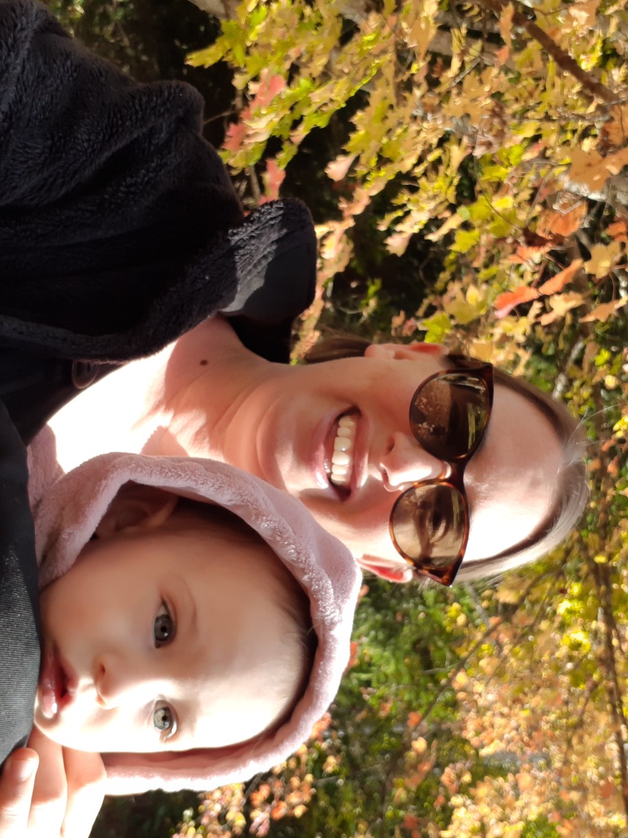 Casey walks outside under fall leaves with her daughter. Case is a white woman with light brown hair who is wearing sunglasses
