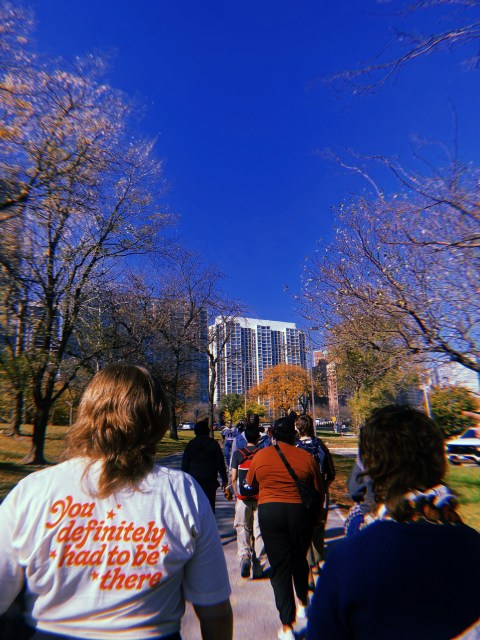 A few queer folks walking along the lakefront in Chicago and a close-up of one of their shirts that says "You definitely had to be there"