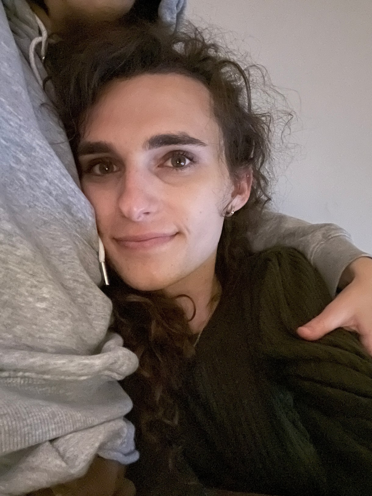 Drew, a white woman with curly hair, cuddles in bed with another person probably her girlfriend