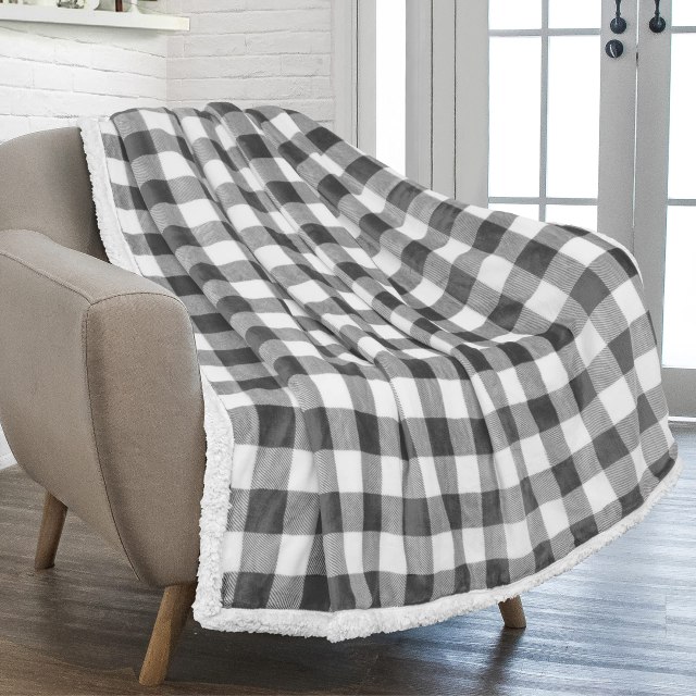 black and white buffalo check draped over gray armchair. there is a white mantle against a white wall and a white paned window