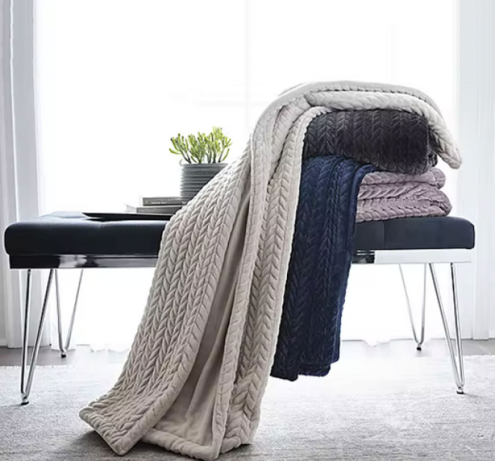 a white chevron knit blanket draped over a black chevron, navy blue and silver chevron blankets on top of a black bench against an open window with a potted plant