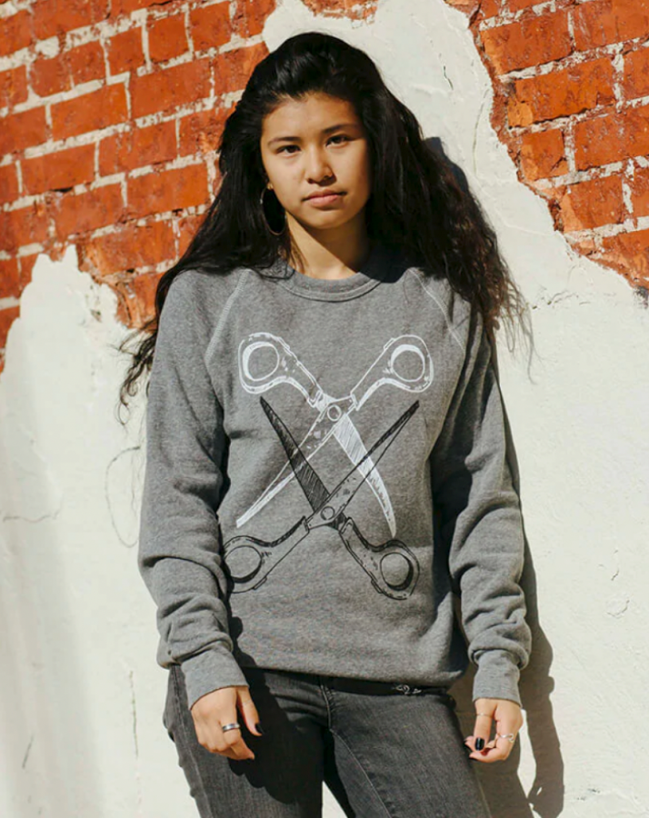 The model Jordan is wearing the grey Basic Scissoring Sweatshirt in size S. The sweatshirt is grey and has a graphic of two scissors, blades open and intertwined. The top scissor is white and the bottom is black.