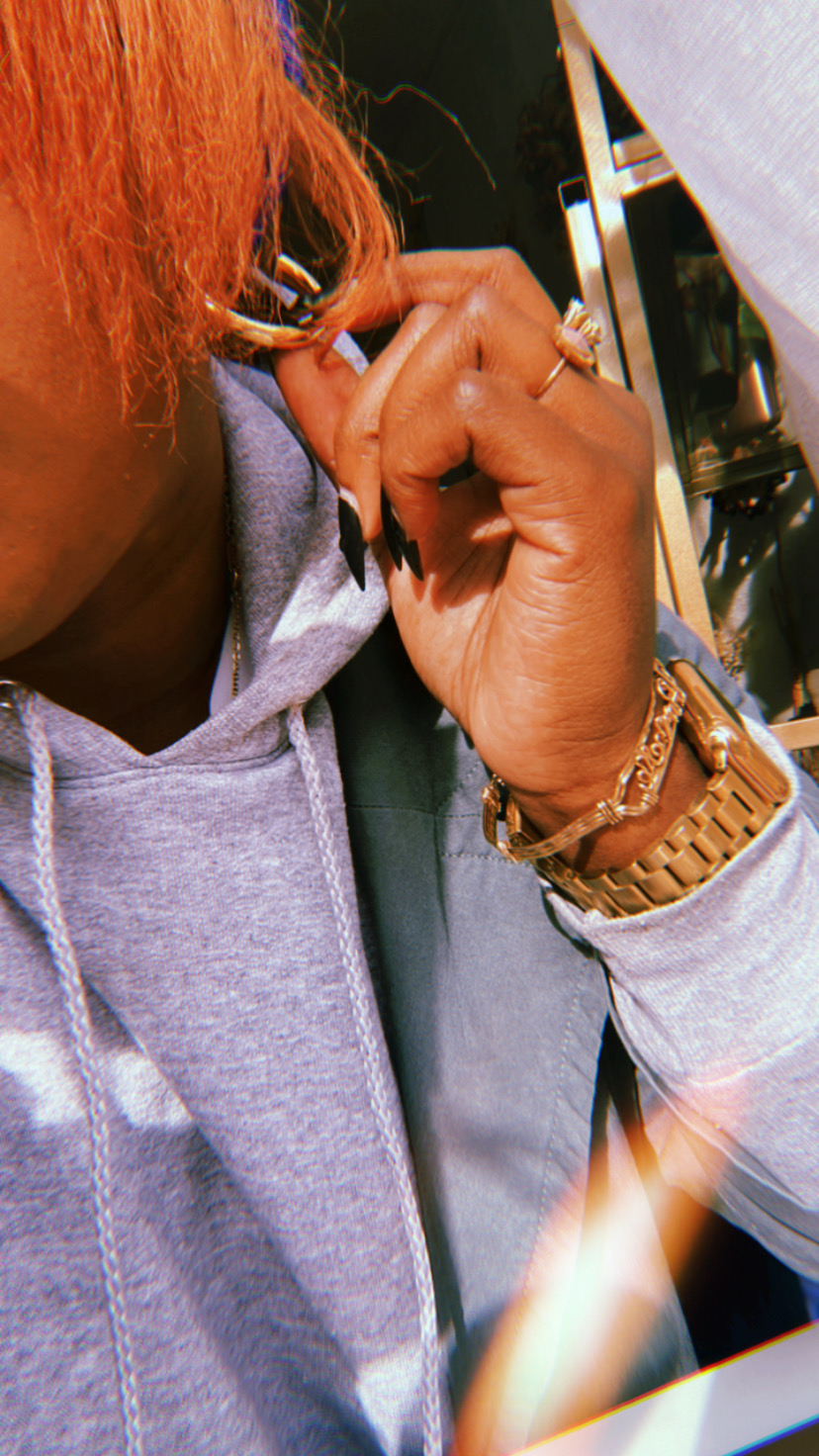 A photo of Shelli in a sweatshirt, playing with her earring. Shelli is also wearing a gold colored wrist watch and bracelet