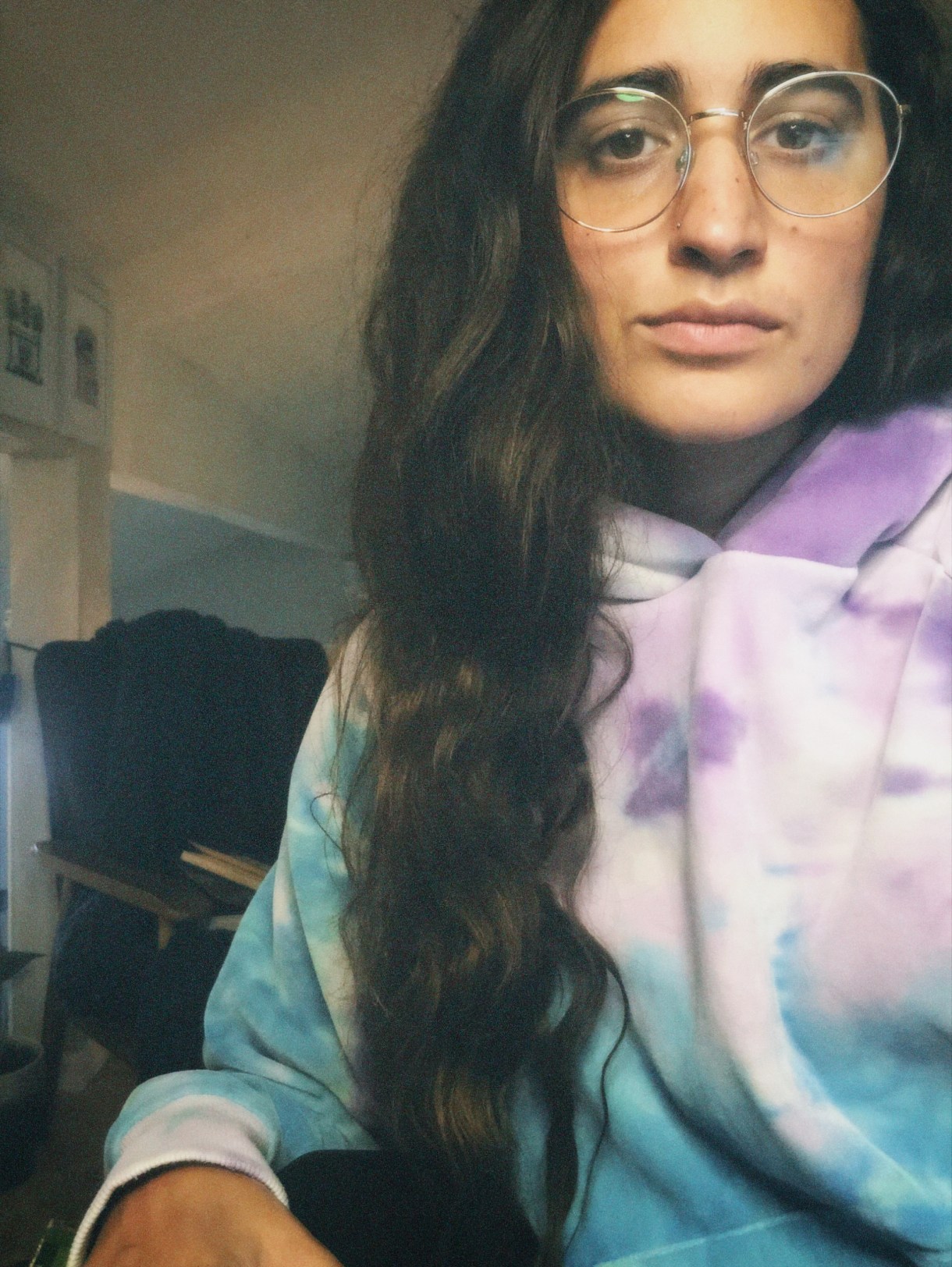 Kayla, a South Asian woman, is wearing a tie dye hoodie and glasses. She has long brown hair.