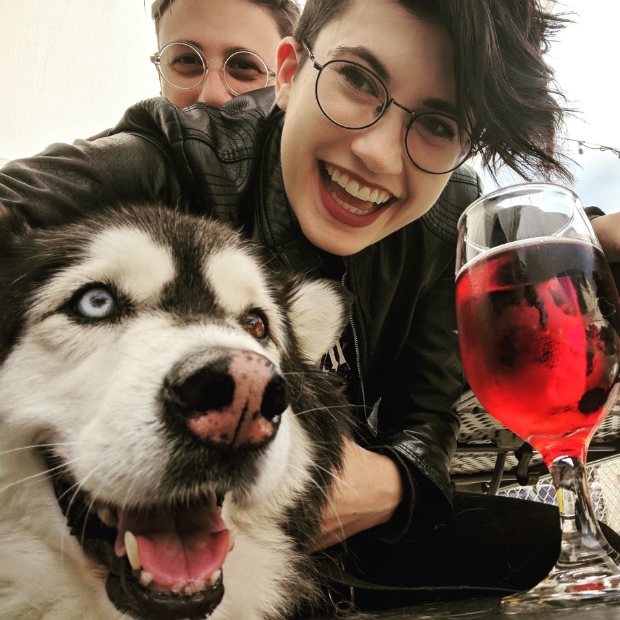 Nico and Sadie smile with Mya the fluffy malaumte mix at a brewery. They all look very happy.