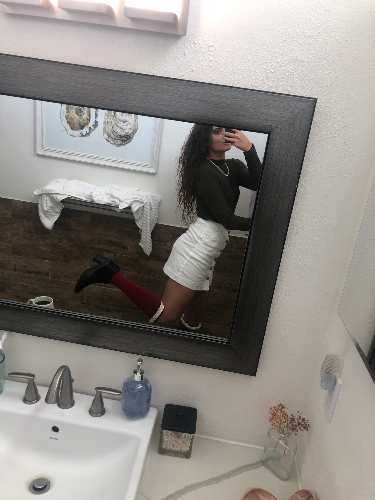 Kayla Kumari Upadhyaya wearing a dark green mock neck sweater and white mini skirt with knee high red socks and black boots.