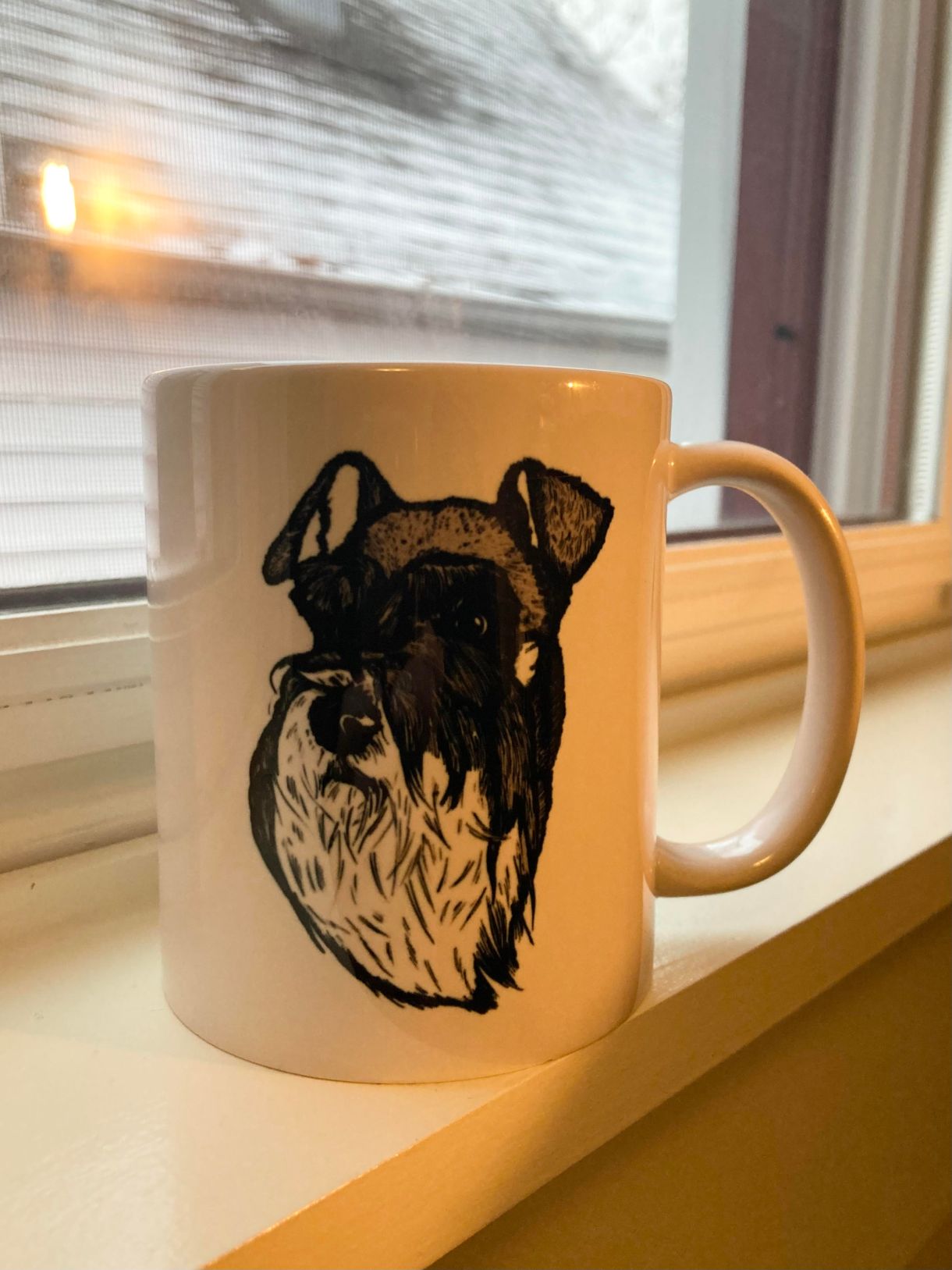 a mug with a schnauzer on it sits on a window ledge