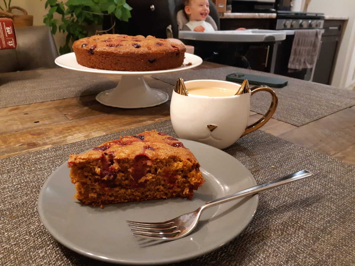 A slice of gingerbread cake on a plate with a cat mug next to it