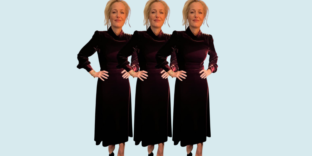 Gillian Anderson wears a dark red velvet dress and has her hands on her hips