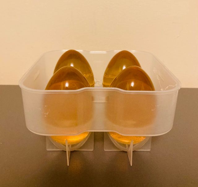 A clear plastic mold containing four, brown gelatin eggs sits on a grey surface against a peach background.