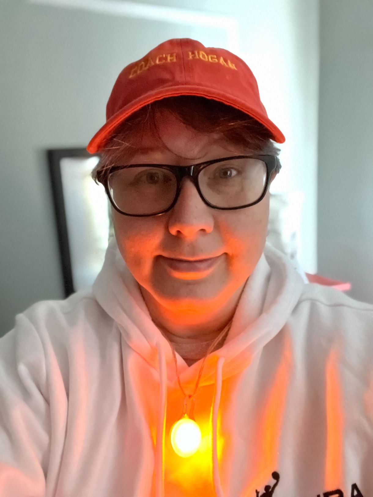 Heather wearing a baseball cap, hoodie, glasses and the glowing LED necklace and smiling