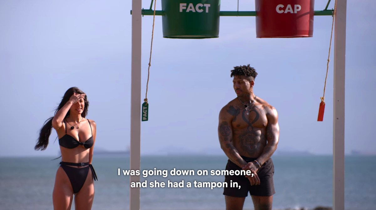 Still from Perfect Match: Francesca Farago in a green bikini standing on the beach next to Dom, who is underneath the two water buckets, dry. The caption reads: "I was going down on someone and she had a tampon in"