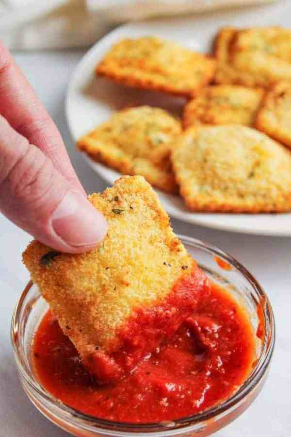 a crispy ravioli being dipped into marinara