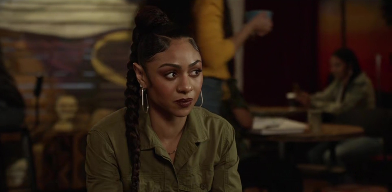 All American: Dressed in an army green jumpsuit, Patience explains to Miko (not pictured) that she has to respect her boundaries. Patience is sitting at Slauson Cafe and their are a couple of indescript customers, in the background, over her left shoulder.