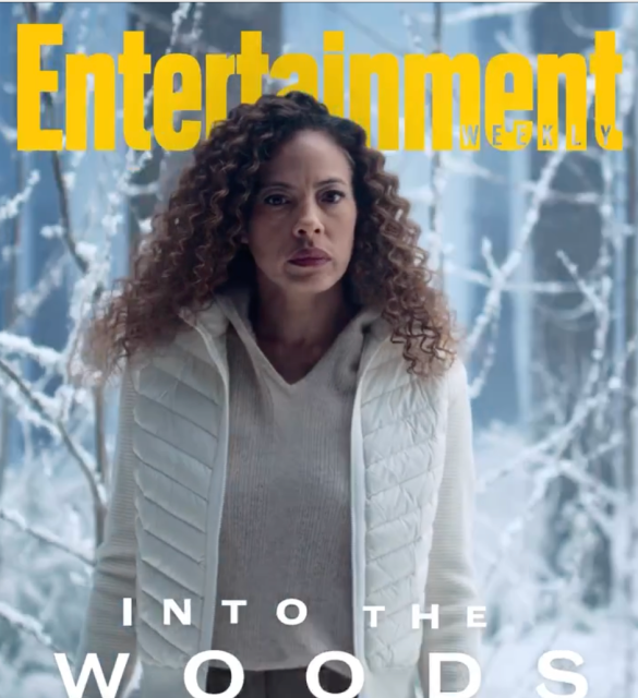 the entertainment cover with tawny cypress, a tall Black woman with long hari, standing in winter clothes in the woods