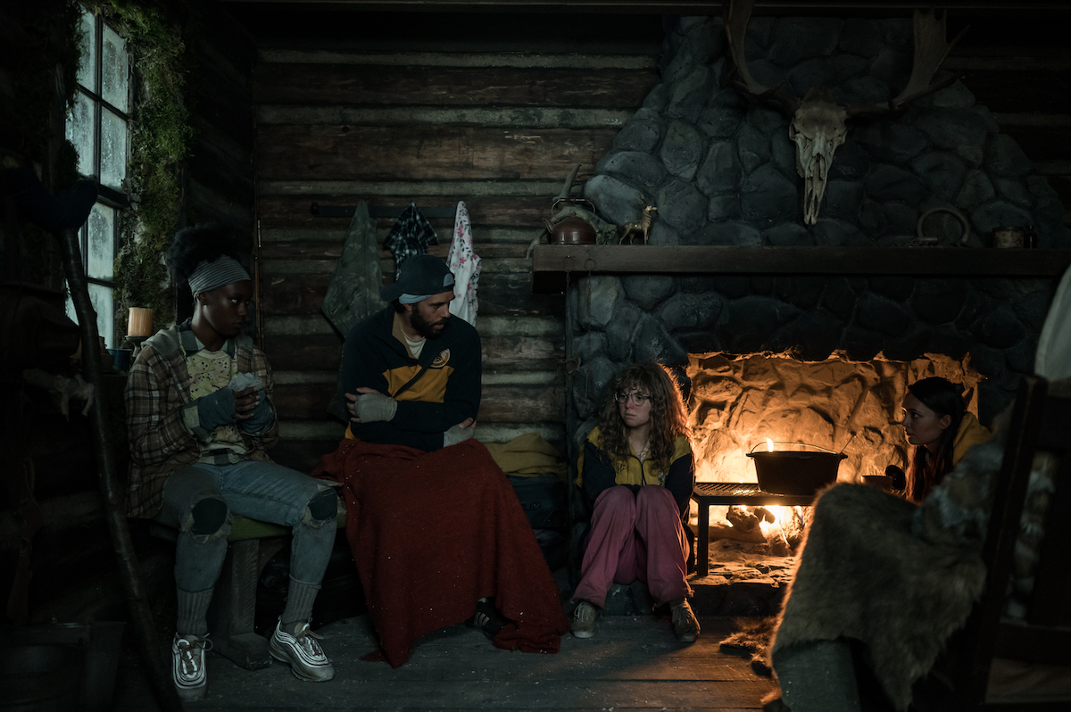 (L-R): Nia Sondaya as Teen Akilah, Steven Krueger as Ben Scott, Samantha Hanratty as Teen Misty, and Alexa Barajas as Teen Mari in YELLOWJACKETS Season 2 sit in a cabin with a fire going. Photo Credit: Kailey Schwerman/SHOWTIME.