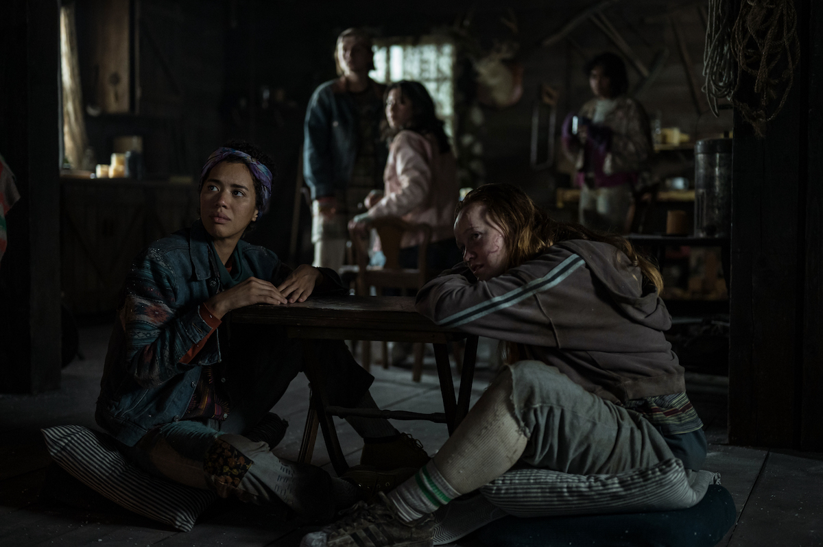 (L-R): Jasmin Savoy Brown as Teen Taissa, Jenna Burgess as Teen Melissa, Mya Lowe as Teen Gen and Liv Hewson as Teen Van in YELLOWJACKETS Season 2 sit on the floor of a cabin. Photo Credit: Kailey Schwerman/SHOWTIME.