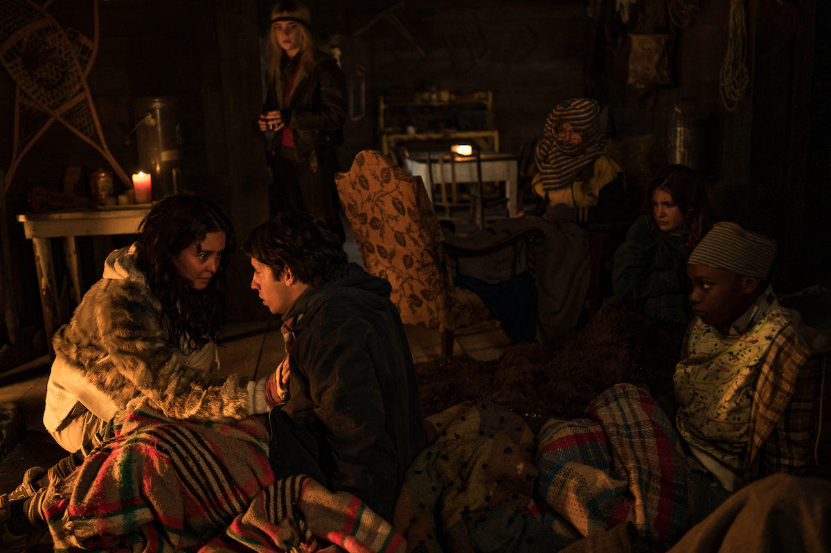 Yellowjackets (L-R): Courtney Eaton as Teen Lottie, Kevin Alves as Teen Travis, Sophie Thatcher as Teen Natalie, Samantha Hanratty as Teen Misty, Sophie Nélisse as Teen Shauna and Nia Sondaya as Teen Akilah in YELLOWJACKETS Season 2 sit in a cabin glowing in fire light. Photo Credit: Kailey Schwerman/SHOWTIME.