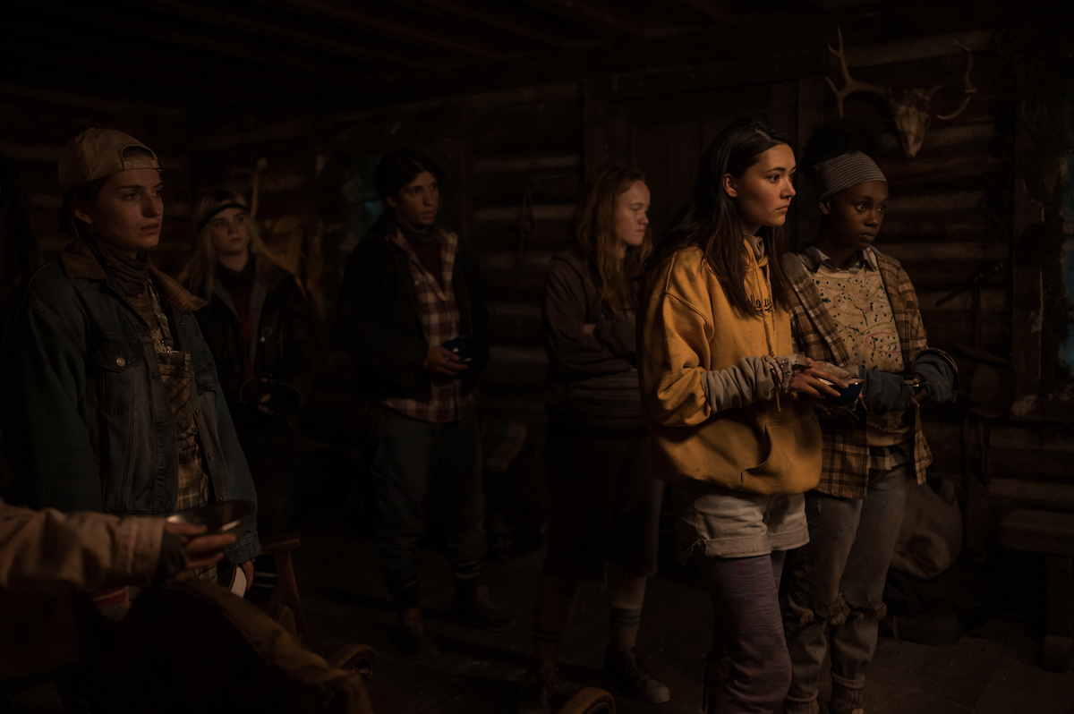 Yellowjackets (L-R): Jenna Burgess as Teen Melissa, Sophie Thatcher as Teen Natalie, Kevin Alves as Teen Travis, Liv Hewson as Teen Van, Alexa Barajas as Teen Mari and Nia Sondaya as Teen Akilah in YELLOWJACKETS Season 2 stand in a group in the cabin. Photo Credit: Kailey Schwerman/SHOWTIME.