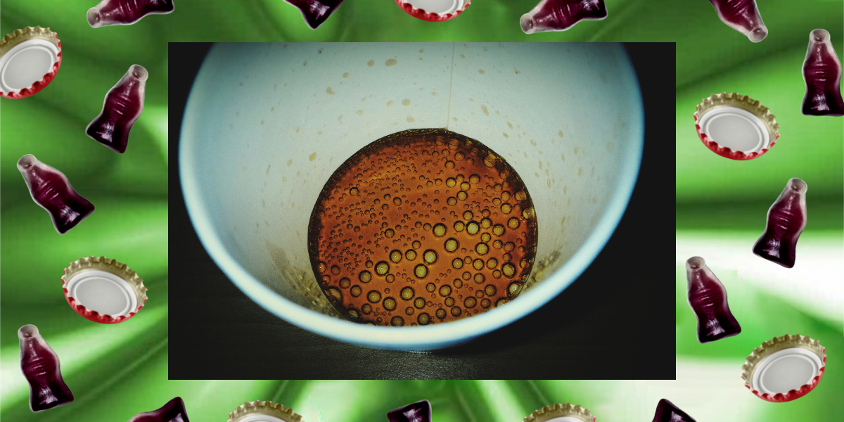 an overhead shot of a nearly empty cup of soda, surrounded by gummy sodas and bottle caps