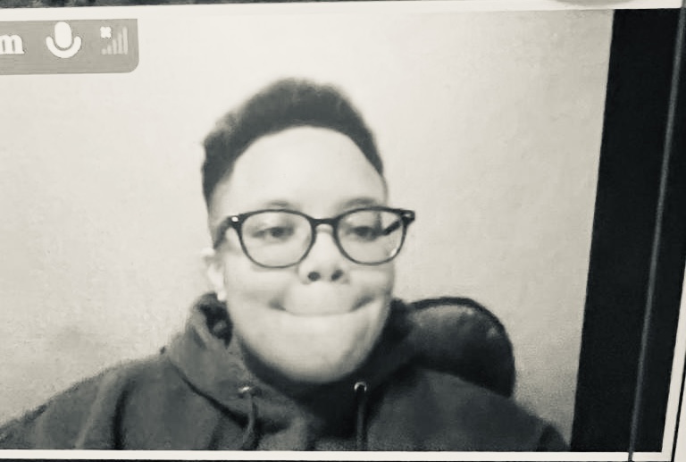 a black and white photo of a.tony, a Black nonbinary person with short hair, shaved sides, and glasses. they are making a funny face and wearing a hoodie