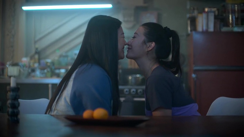 Alice (L) and Sumi (R) lean in for a kiss at the Coterie table. Alice is still in her pajamas and Sumi is wearing her scrubs for work.