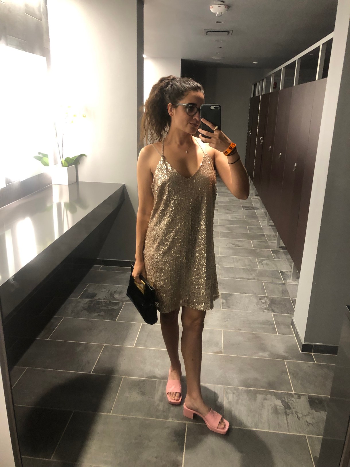 Kayla Kumari Upadhyaya in a gold sleeveless dress with a black clutch and pink heeled slides.