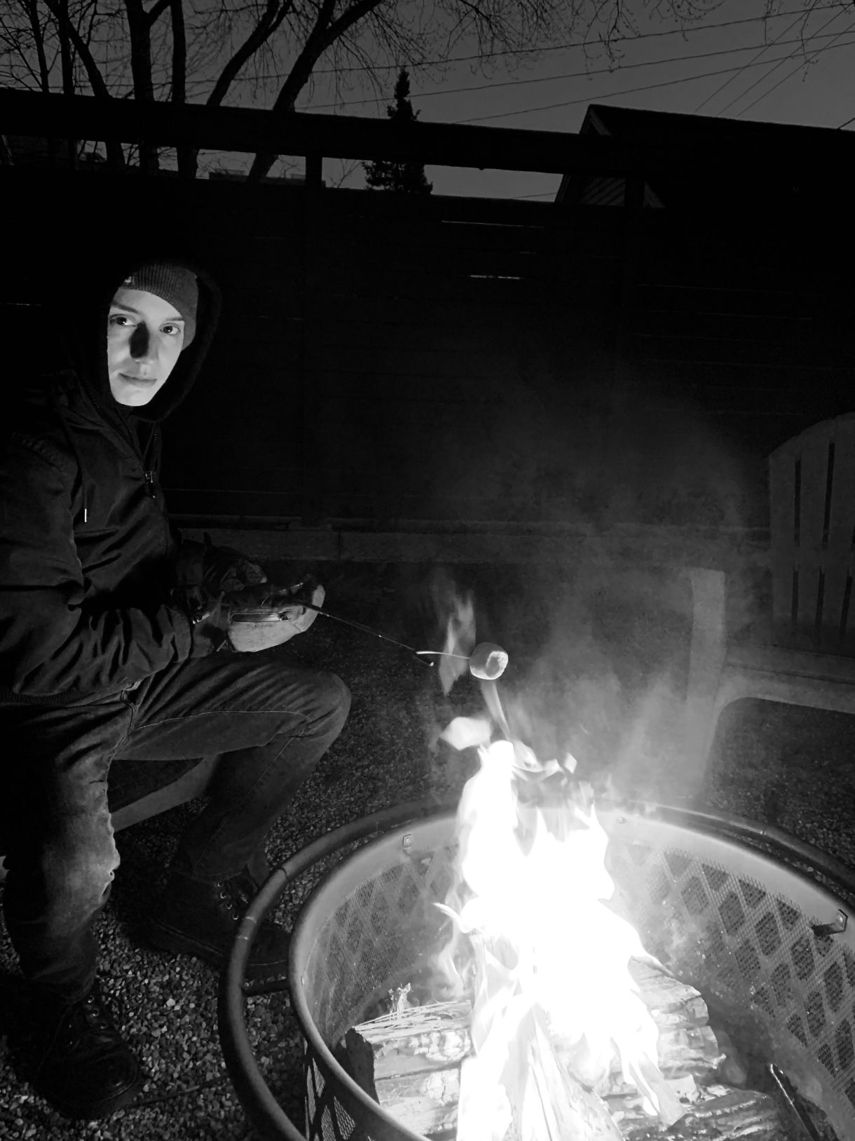 a black and white photo of ro a white person, sitting near a fire outside