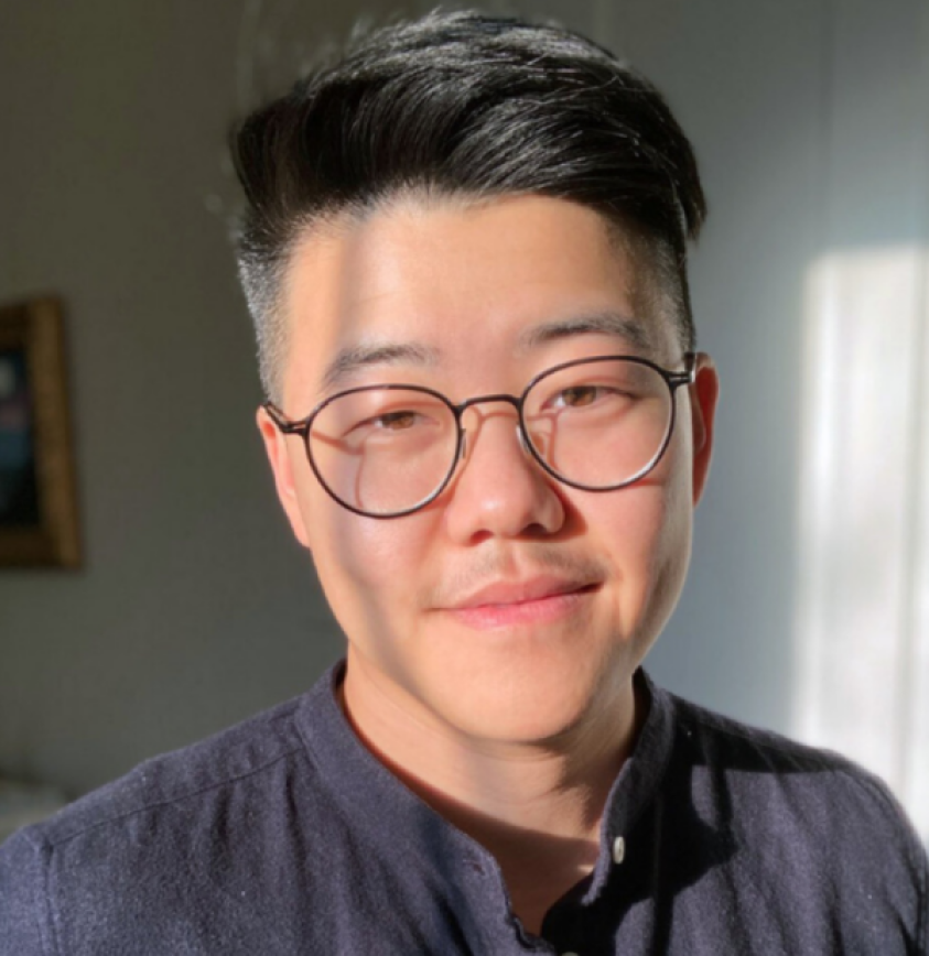 portrait of Yanyi, an Asian American person with black hair and glasses, smiling softly at the viewer. He is wearing a grey shirt and a soft white background is behind him.