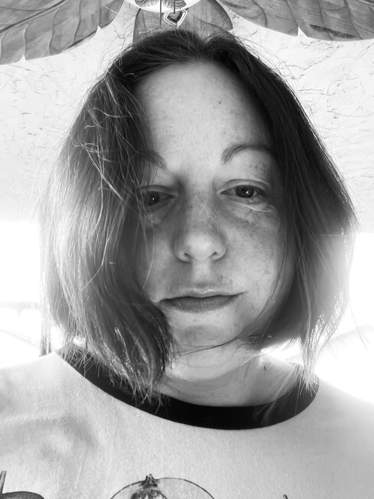 a black and white photo of Darcy, a white person, with a bob, backlit by a window, looking moody