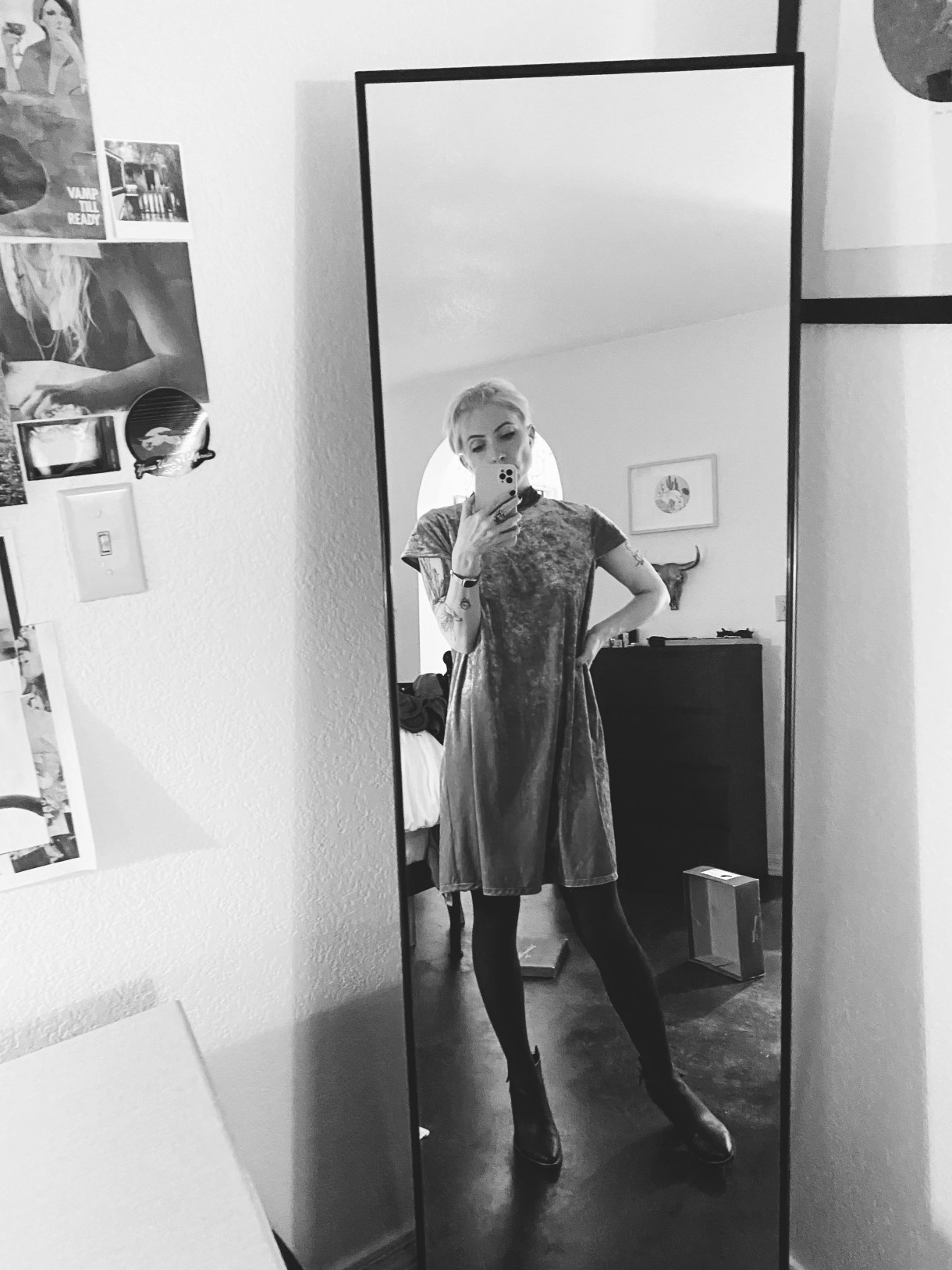 a black and white photo of Laneia a white woman taking a mirror selfie. she is wearing a dress and is seen from far away