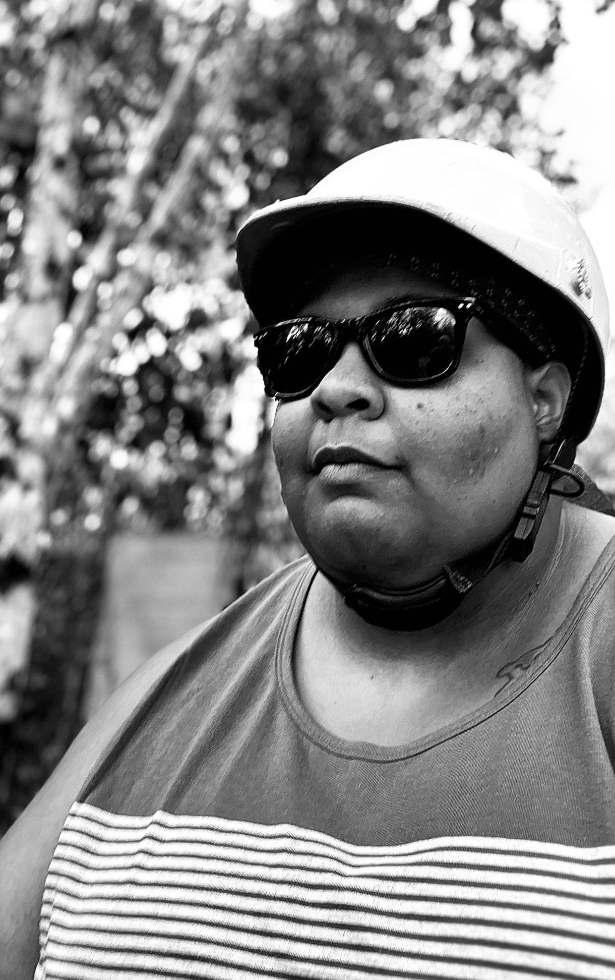 a black and white photo of shea, a Black human, wearing a helmet and sunglesses, looking serious out of doors