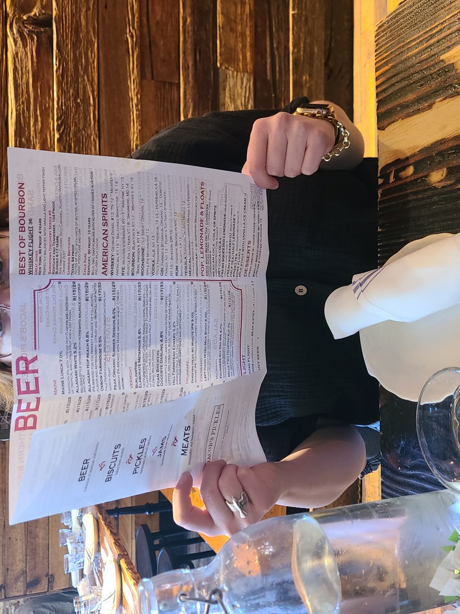 Jess, a white woman with glasses and a baseball cap, holds a menu at Jacob's Pickles