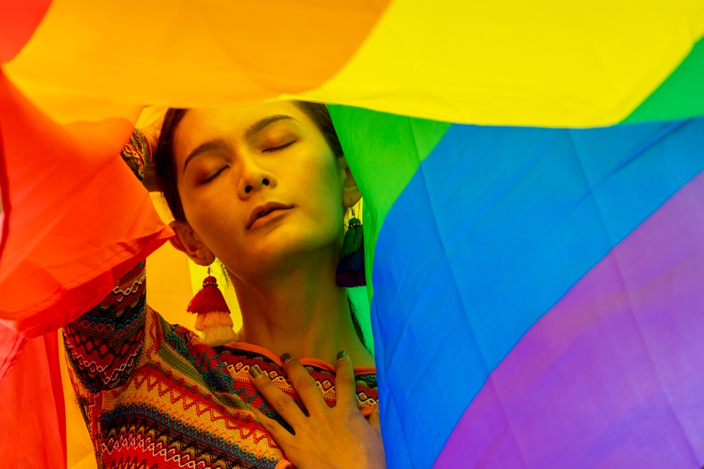 An eleganct transgender woman in a colorful rainbow flag costume is dancing in a parade for LGBTQ+ pride month.