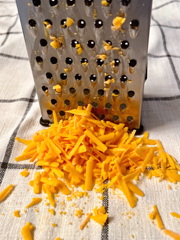 a pile of yellow grated cheese and a cheese grater.