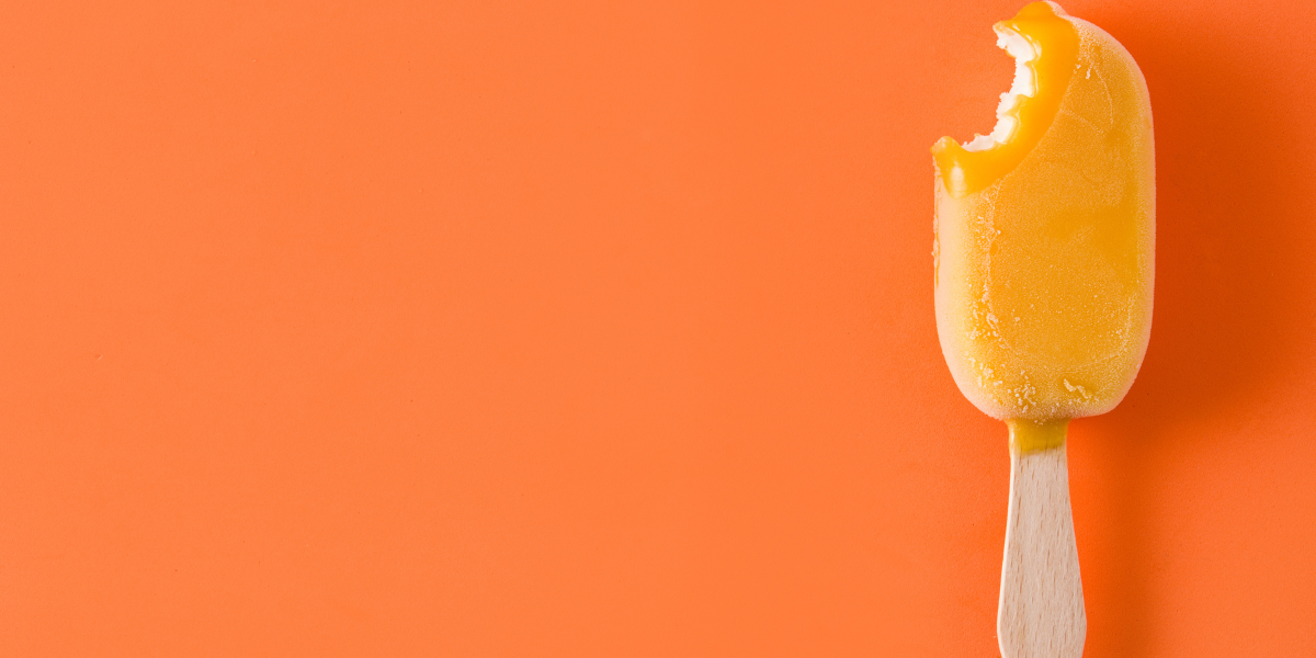 a creamsicle with a bite taken out of it against an orange background