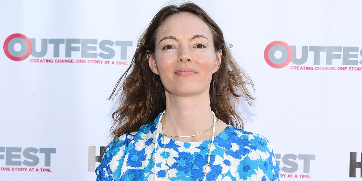 Stewart Thorndike is in a blue print dress while smiling on the Outfest red carpet.