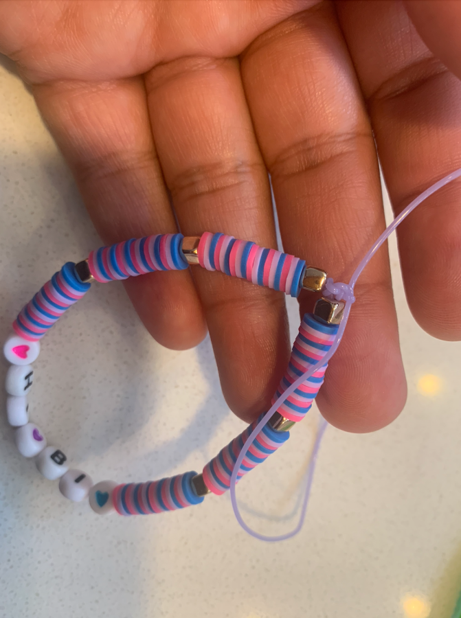 A knotted bracelet that says HI BI with pink, purple, and blue clay beads