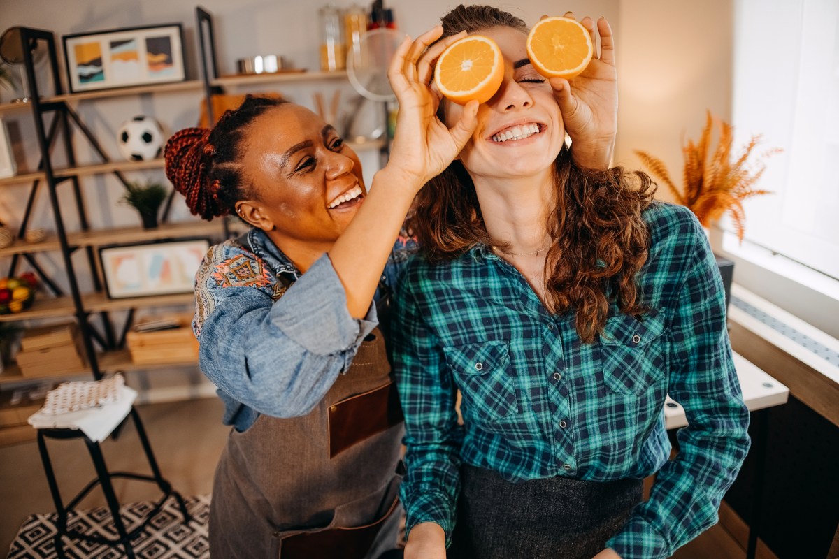 a woman holds orange halves up in front of her girlfriend's eyes