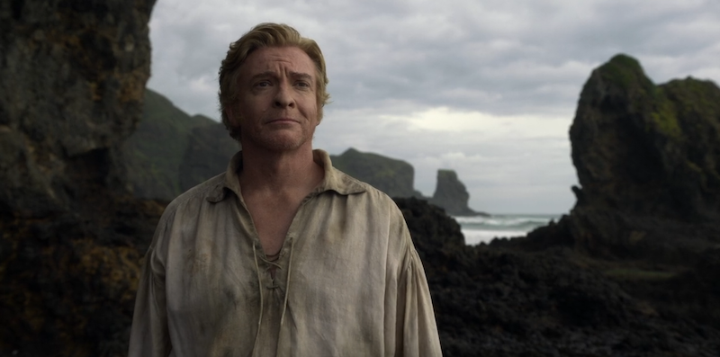 Stede Bonnet wearing a dirty white shirt, staring off into the middle distance, with rocks and ocean behind him.