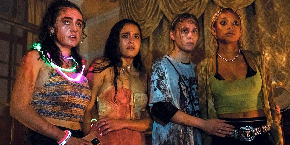 four teens in the movie Bodies Bodies Bodies, covered in blood and sweat and wearing glow in the dark necklaces look at something in horror