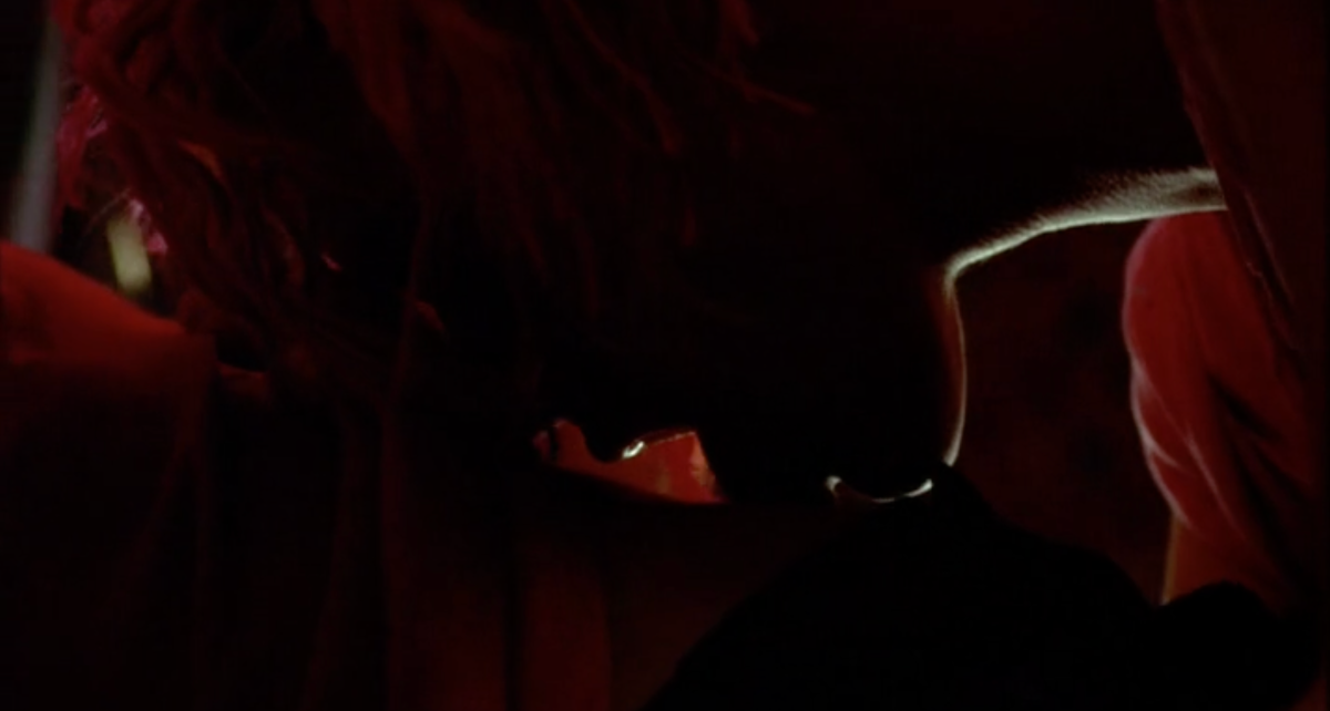 Sexy lesbian screenshot: Leisha Hailey with pink hair in very low lighting licks another woman's back.