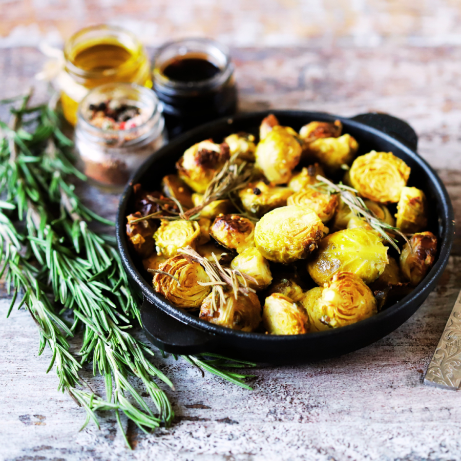 brussels sprouts in a cast iron pan with balsamic and oil on the side and rosemary