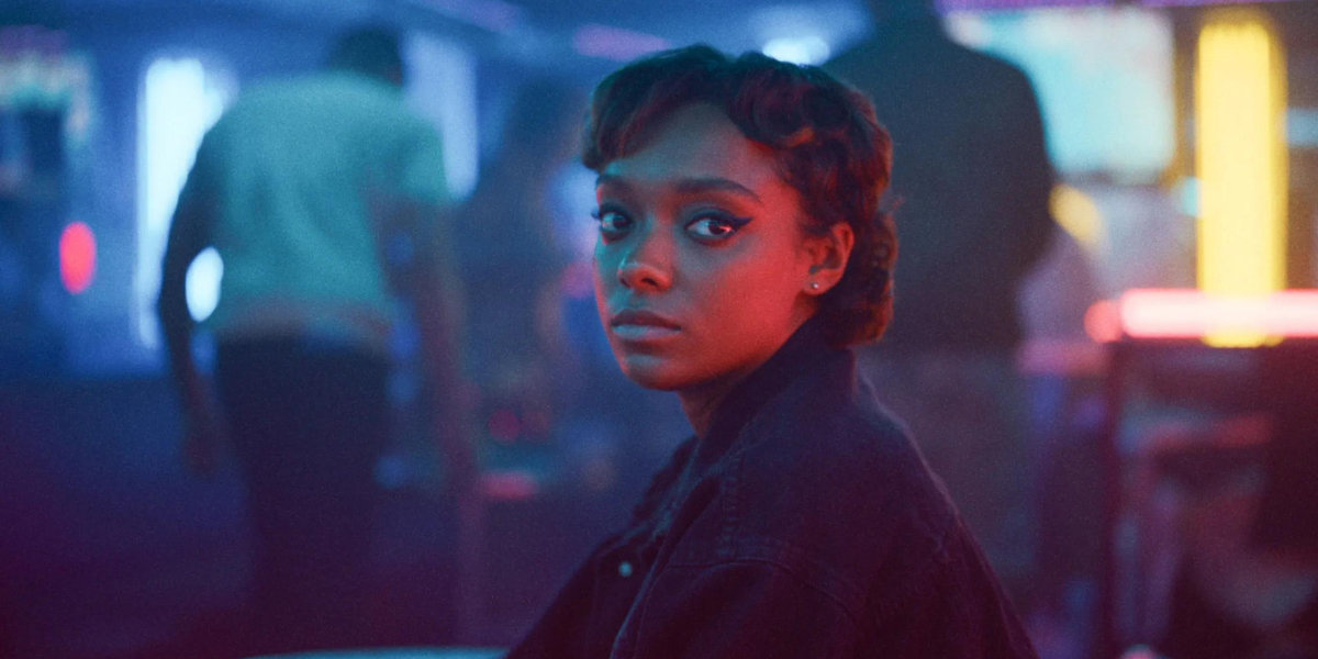 Sophie Wilde stares toward the camera in red and blue light and soft focus.