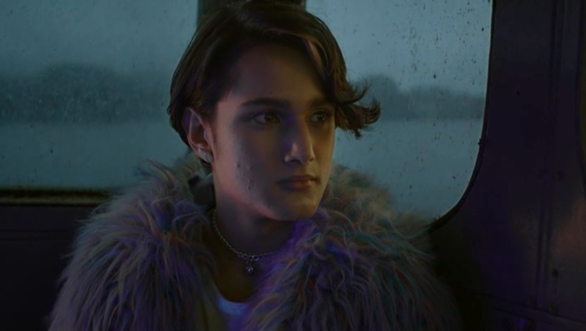 A close up on a trans teenage girl with short hair and a feathered rainbow collar. 